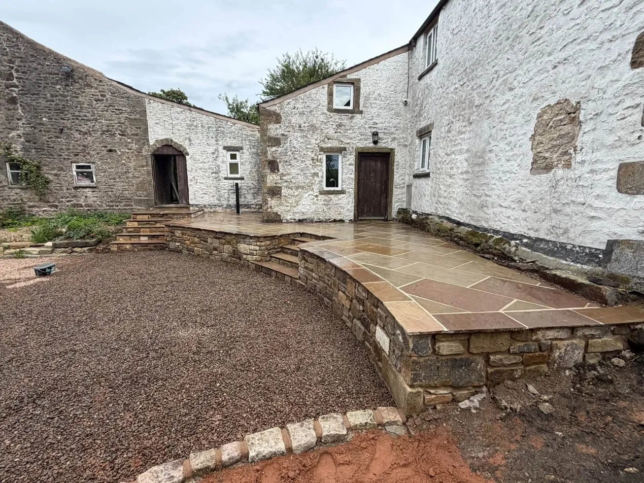 Finished stone flag patio with curved retaining wall and steps at a whitewashed stone building